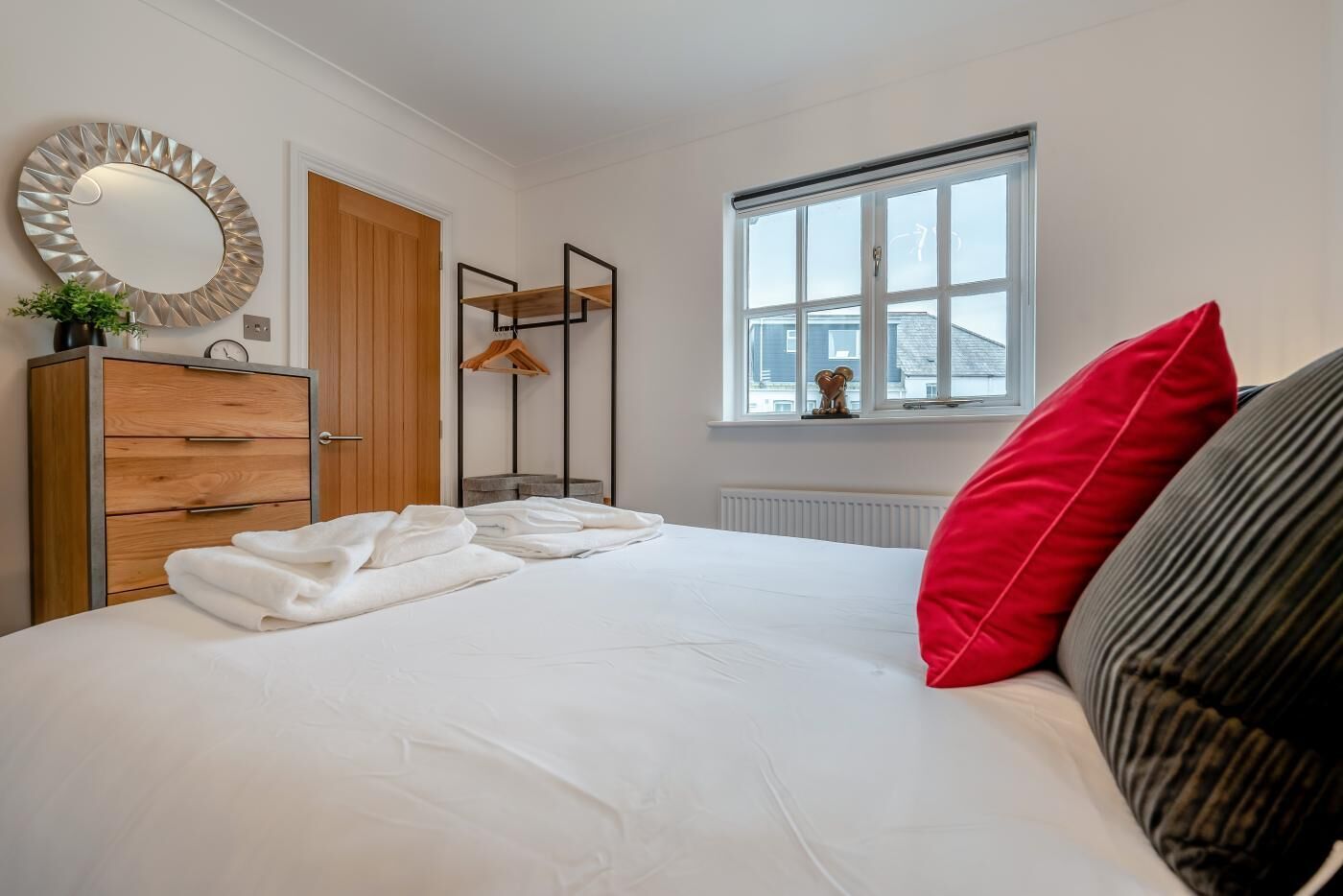 Ein Schlafzimmer mit einem Bett, einem Holzschrank, einem Spiegel, einem Fenster mit Blick und einer Heizung.