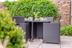 An outdoor dining area with wicker furniture and a table set with white dishes and a vase of flowers. - 3 Bed in Padstow (oc-c28137) (Padstow)