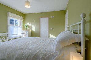 Ein Schlafzimmer mit Bett, Nachttisch, Fenster mit Vorhängen und einer Tür.