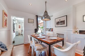 Un comedor con mesa de madera, sillas blancas y una lámpara colgante.