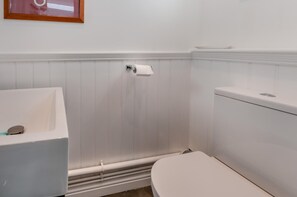 Un baño con lavamanos blanco, inodoro y dispensador de papel higiénico en la pared.