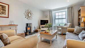 A cozy living room with a fireplace, comfortable seating, a television, and a large window. - 3 Bed in St. Breward (oc-g28144) (Saint Breward)