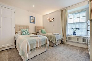 A bedroom with two beds, a radiator, a window with curtains, and a wall-mounted light fixture.