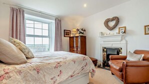 A bedroom with a bed, a fireplace, a leather armchair, and a window with curtains. - 3 Bed in St. Breward (oc-g28144) (Saint Breward)
