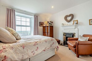 Un dormitorio con cama, chimenea, sillón de cuero y ventana con cortinas.