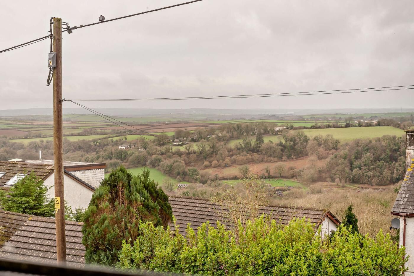A rural landscape with a house, power lines, and a cloudy sky.