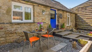 A stone building with a blue door, a small outdoor seating area with wicker chairs and a table, and a garden with potted plants. - 1 Bed in St. Tudy (oc-t28171) (Michaelstow)
