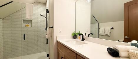 A modern bathroom with a glass shower, a large mirror, and a wooden vanity.