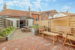 A patio area with a brick floor, wooden furniture, and a covered seating area. - 3 Bed in Southwold (oc-r11173) (Southwold)
