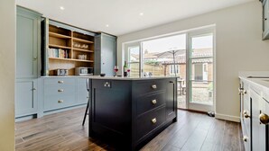 A modern kitchen with grey cabinets, a black island, and a large window offering a view of the backyard. - 3 Bed in Southwold (oc-r11173) (Southwold)
