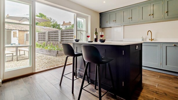 A modern kitchen with a large island, bar stools, and a view of the garden through the sliding doors. - 3 Bed in Southwold (oc-r11173) (Southwold)