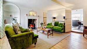 A living room with a fireplace, green sofas, and a dining area with a table and chairs. - 3 Bed in Southwold (oc-r11173) (Southwold)