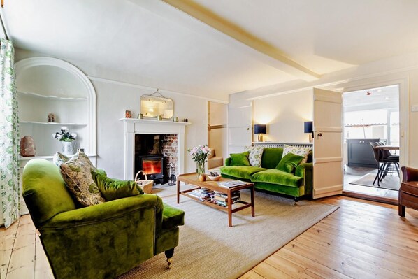 A living room with a fireplace, green sofas, and a dining area with a table and chairs. - 3 Bed in Southwold (oc-r11173) (Southwold)
