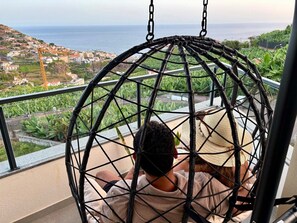 A person sitting in a spherical hanging chair with a view of a coastal town and the sea. - GuestReady - Seaview Escape (Câmara de Lobos)