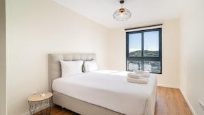A modern bedroom with a large bed, a round side table, a unique geometric pendant light, and a large window with a city view. - GuestReady - Seaview Escape (Câmara de Lobos)