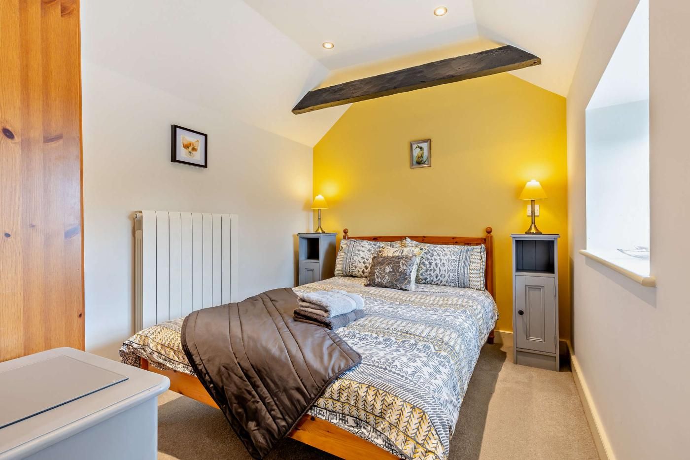 A bedroom with a bed, bedside tables, a radiator, and a window.