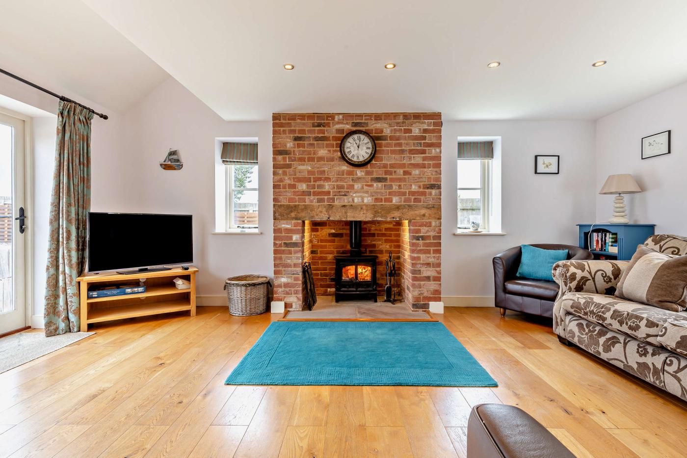 A living room with a brick fireplace, a television on a wooden stand, a blue rug, and a sofa with patterned cushions.