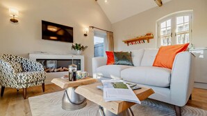 A living room with a sofa, armchair, coffee table, fireplace, and a television mounted on the wall. - 1 Bed in Market Weston (oc-t27890) (Market Weston)