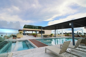 Una piscina al aire libre, sombrillas, sillones reclinables de piscina