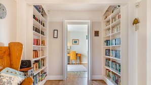 A narrow hallway with bookshelves on both sides, leading to a room with a desk and chair. - 4 Bed in West Bexington (oc-s28233) (West Bexington)