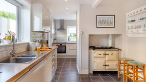 A modern kitchen with a large island, built-in oven, and a small dining area with stools. - 4 Bed in West Bexington (oc-s28233) (West Bexington)
