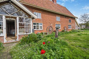 A traditional brick house with a large front porch, a garden with flowers, and two large wooden wheels. - 3 Bed in Rumburgh (oc-c27094) (Rumburgh)