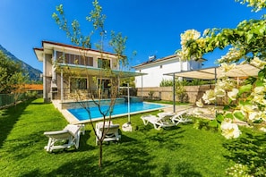 Ein zweistöckiges Haus mit Swimmingpool, überdachter Terrasse und gepflegtem Rasen.