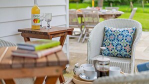 An outdoor seating area with wicker furniture, a table with a bottle of OWTLE Kent Apple 2013, two glasses, and a tray with cups and a coffee pot. - 3 Bed in Marden (oc-w28286) (Horsmonden)
