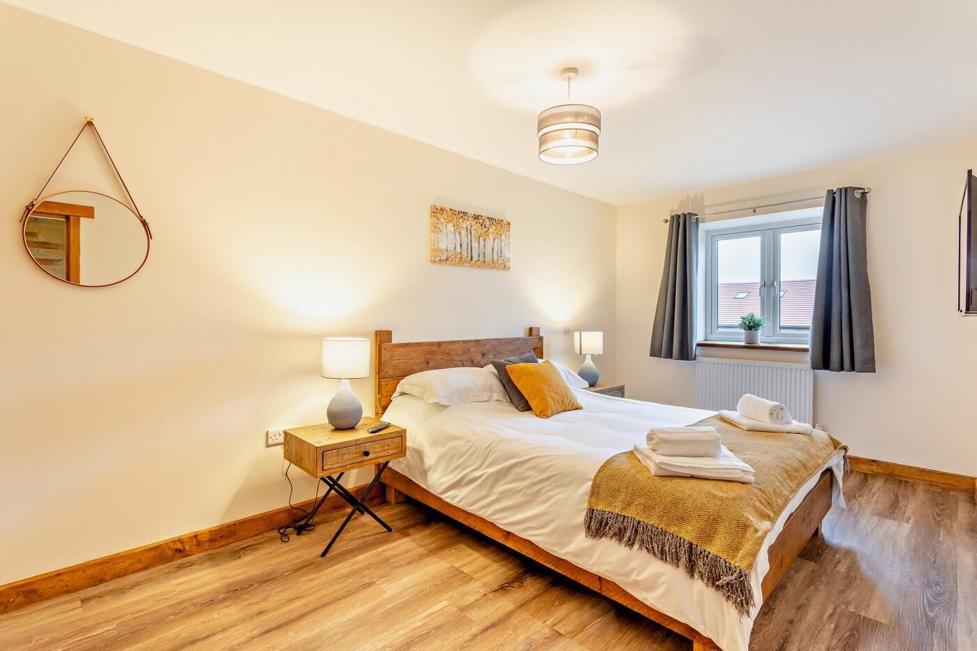 A bedroom with a wooden bed, bedside lamps, a mirror, a window with curtains, and a ceiling light.