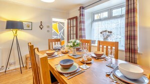 Une salle à manger avec une table en bois dressée pour quatre personnes, un lampadaire et une fenêtre avec des rideaux.