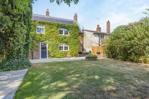 A house with a brick exterior partially covered in ivy, a front door, and a small patio area with a table and chairs. - 4 Bed in East Rudham (oc-t28312) (East Rudham)