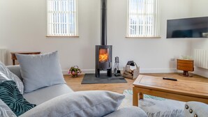 Een moderne woonkamer met een centrale houtkachel, een bank, een salontafel en een televisie aan de muur.