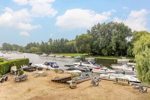 Ein Yachthafen mit vertäuten Booten, eine Rasenfläche mit Sitzgelegenheiten und ein Fluss.