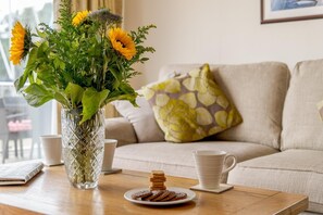 Ein Zimmer mit einer Couch, einem Couchtisch mit Blumen in einer Vase, einem Teller Kekse und einer Tasse.