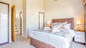 Una camera da letto con un letto, lampade da comodino, un comodino, una porta e una scala.