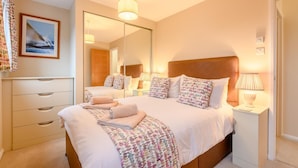 Ein helles Schlafzimmer mit einem großen Bett, Nachttischen, einem Spiegel und einer Kommode.