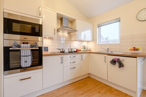 Eine moderne Küche mit weißen Schränken, einem Edelstahlbackofen, einem Fenster und einer Uhr an der Wand.