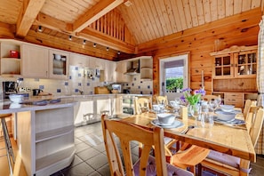 A wooden cabin interior with a kitchen, dining area, and a view of greenery outside. - 3 Bed in Little Petherick (oc-c28311) (Little Petherick)