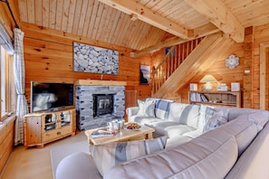 A cozy cabin interior with a stone fireplace, a television, a sofa, and a bookshelf. - 3 Bed in Little Petherick (oc-c28311) (Little Petherick)