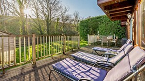 A deck with lounge chairs and a table, surrounded by a wooden fence and greenery.