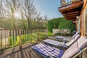 A deck with lounge chairs and a table, surrounded by a wooden fence and greenery. - 3 Bed in Little Petherick (oc-c28311) (Little Petherick)