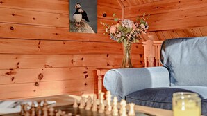 A wooden cabin interior with a chessboard, a sofa, a vase with flowers, and a framed picture of a puffin.