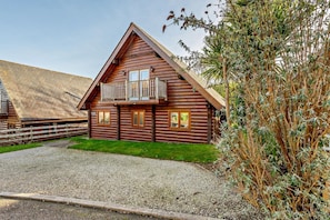 A log cabin with a balcony, a gravel driveway, and a fenced area. - 3 Bed in Little Petherick (oc-c28311) (Little Petherick)
