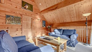 A cozy wooden interior with a sofa, a table with chess, and a lamp.