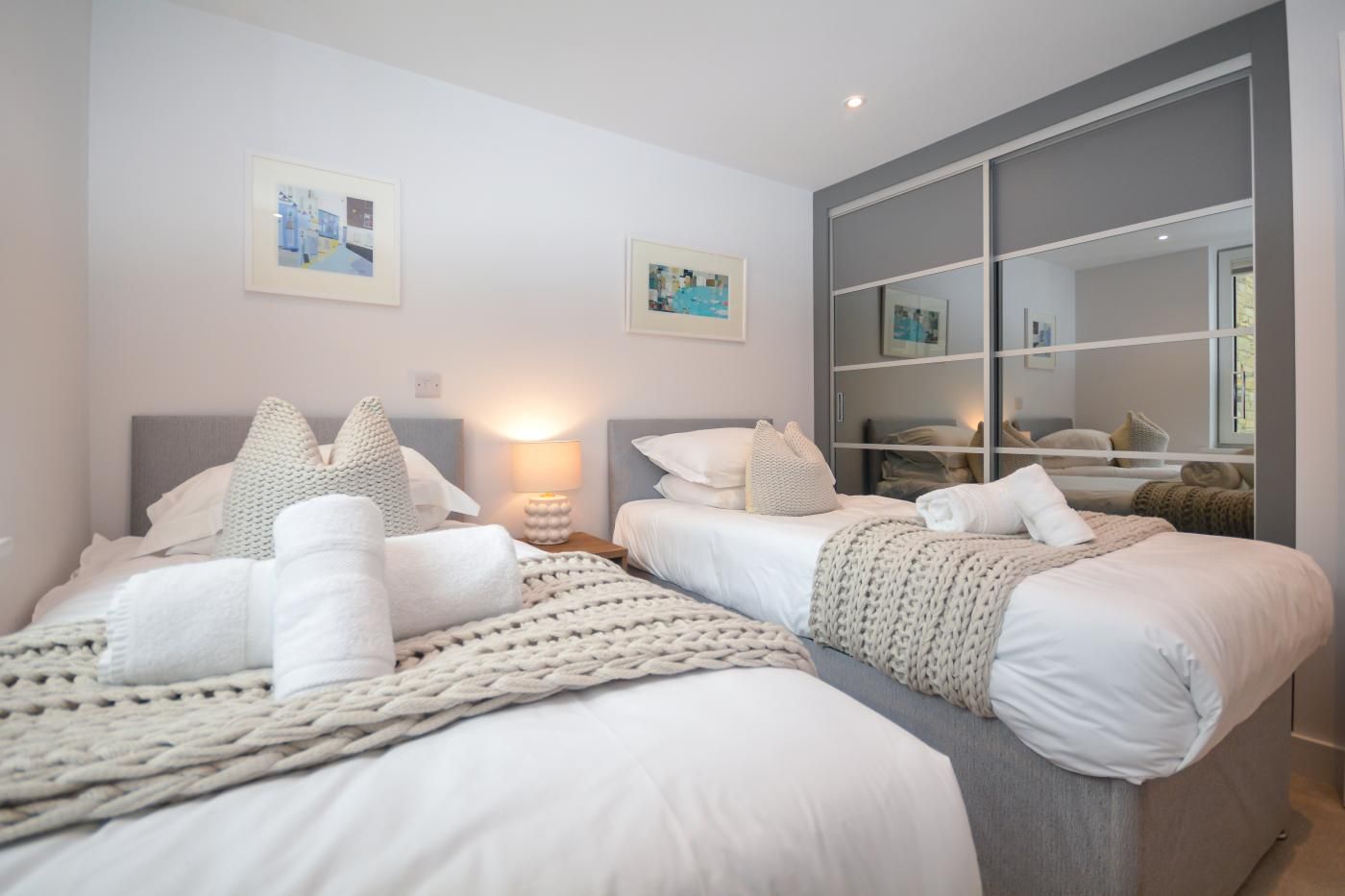 A modern bedroom with two beds, a large mirror, and artwork on the walls.
