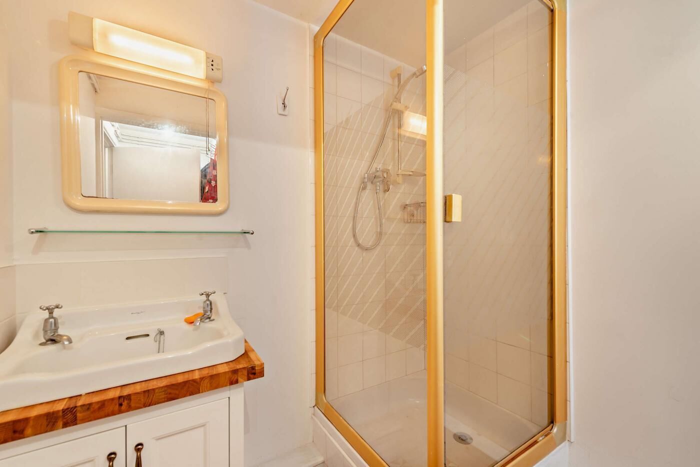 A bathroom with a wooden vanity, a glass shower enclosure, and a mirror with lights.