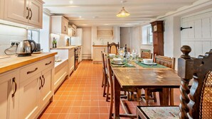 Une cuisine avec des meubles blancs, une table à manger en bois pour six personnes et un sol carrelé.
