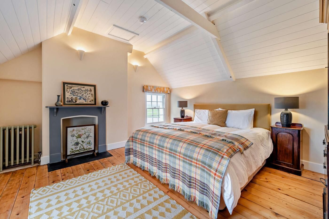 A bedroom with a large bed, a fireplace, a nightstand, and a lamp.