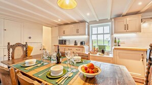 A well-lit kitchen with wooden cabinets, a dining table set with plates, glasses, and a bowl of fruit. - 2 Bed in Southgate (oc-p28298) (Southgate)