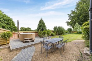 Une terrasse extérieure avec un bain à remous en bois, une table avec des chaises et un chemin en briques.